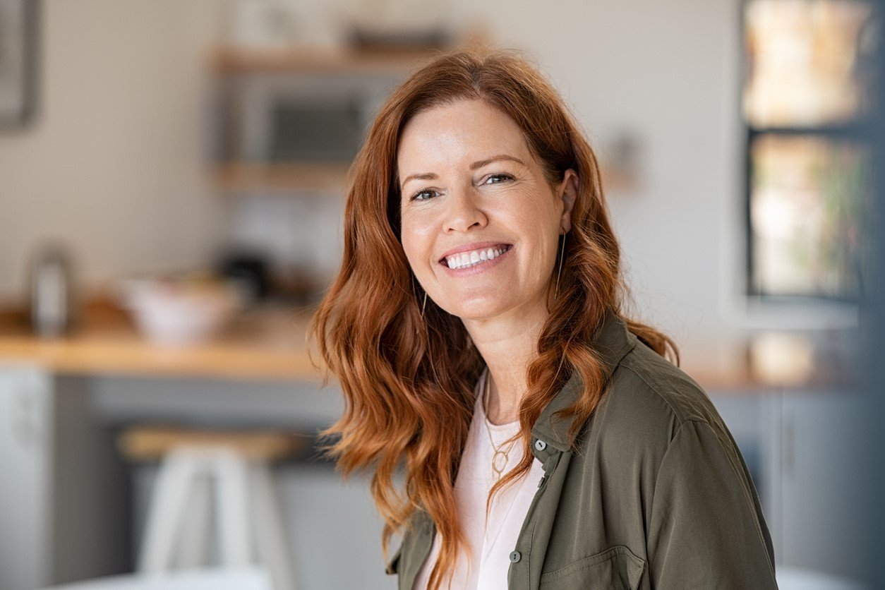 Life Extension, a middle-aged red-haired, smiling, relaxed, and vital looking woman with a kitchen in the background